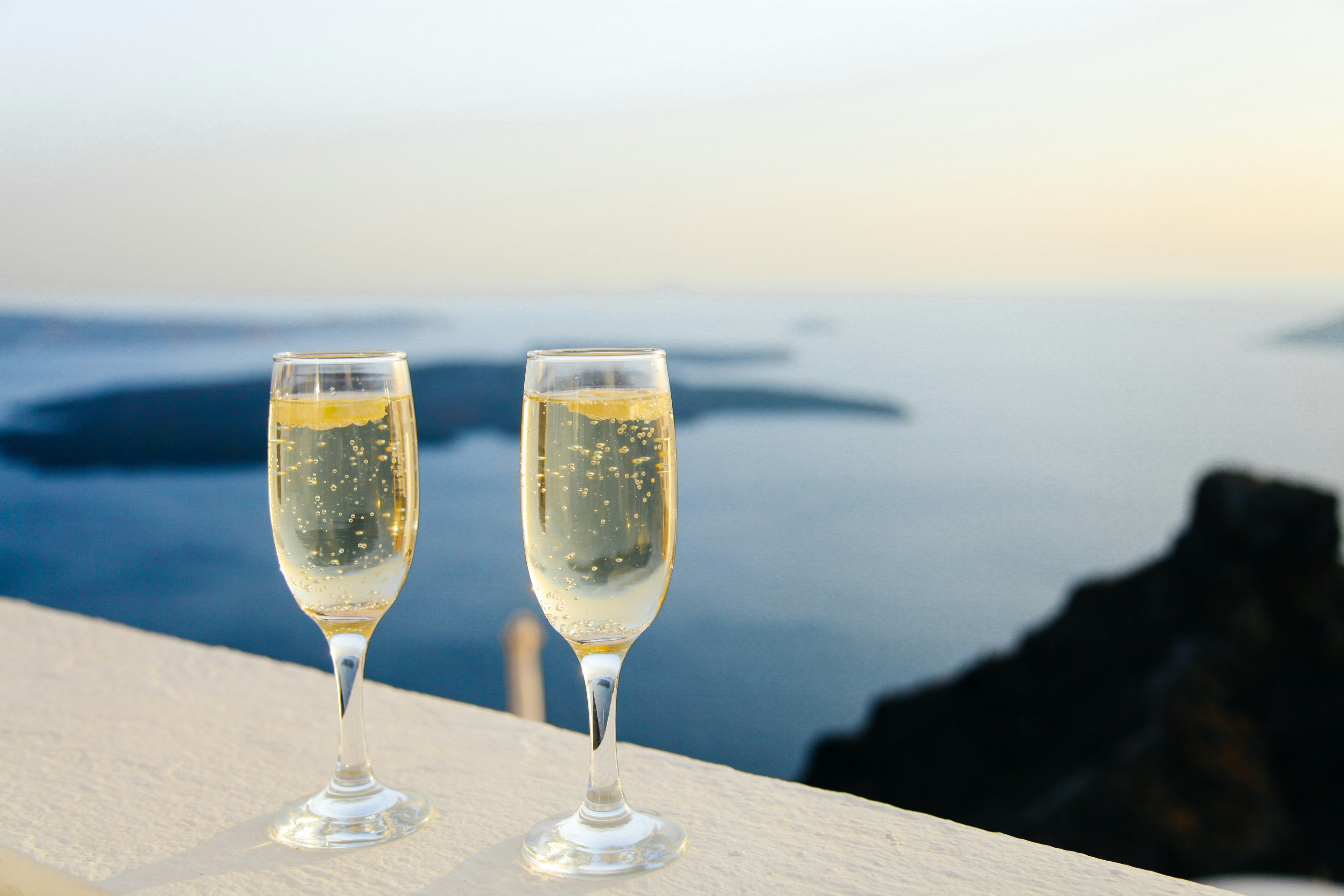Zwei mit Sektgläser, die mit entalkoholisierten Sekt gefülllt sind und auf einer Fensterbank stehen. Im Hintergrund das Meer. 